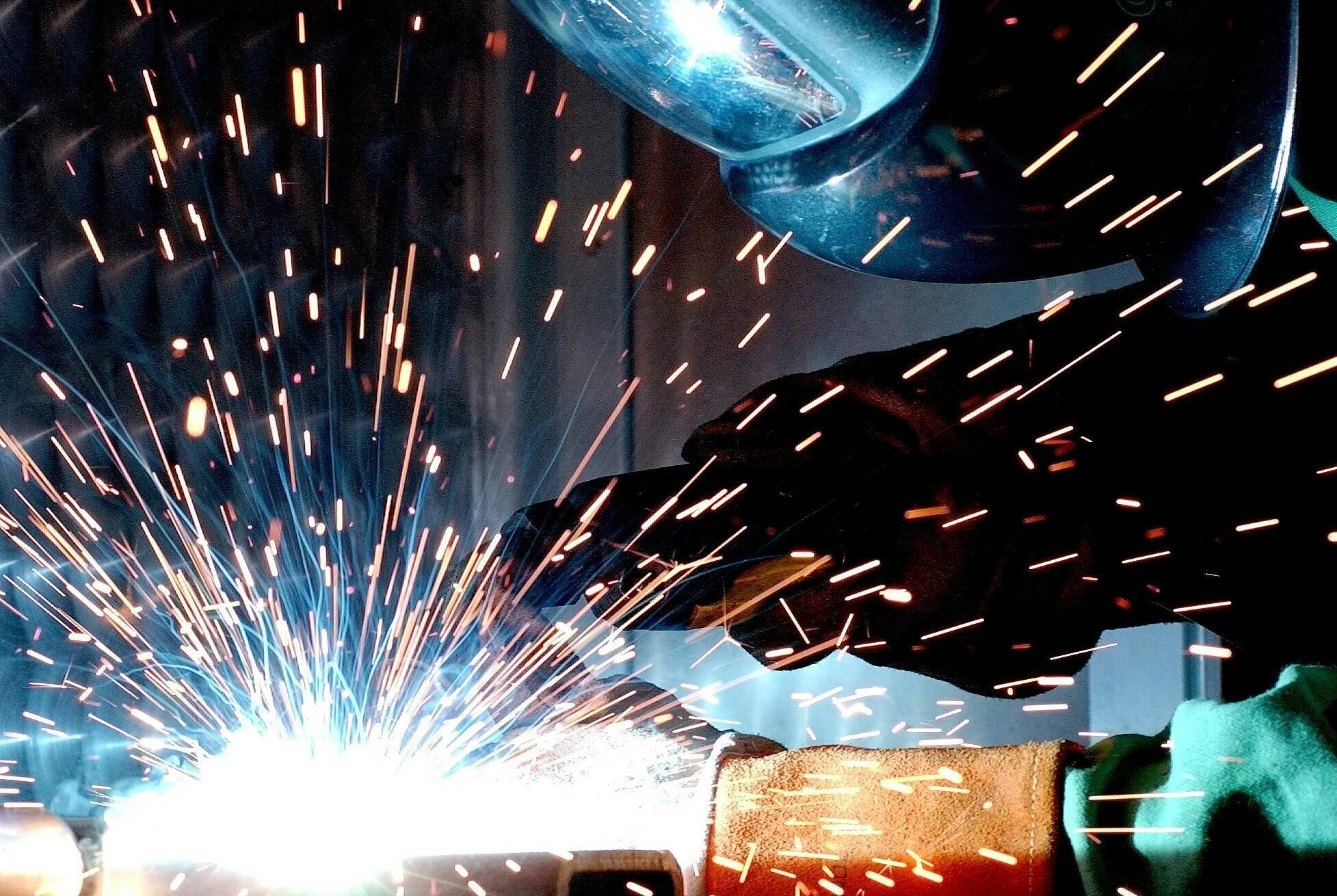 A focused welder works with metal in an industrial setting, creating vibrant sparks.